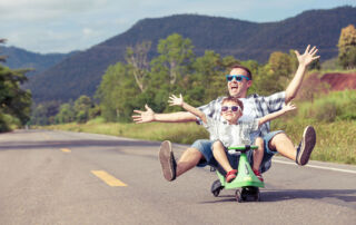 Father and son having fun riding a scooter down the road